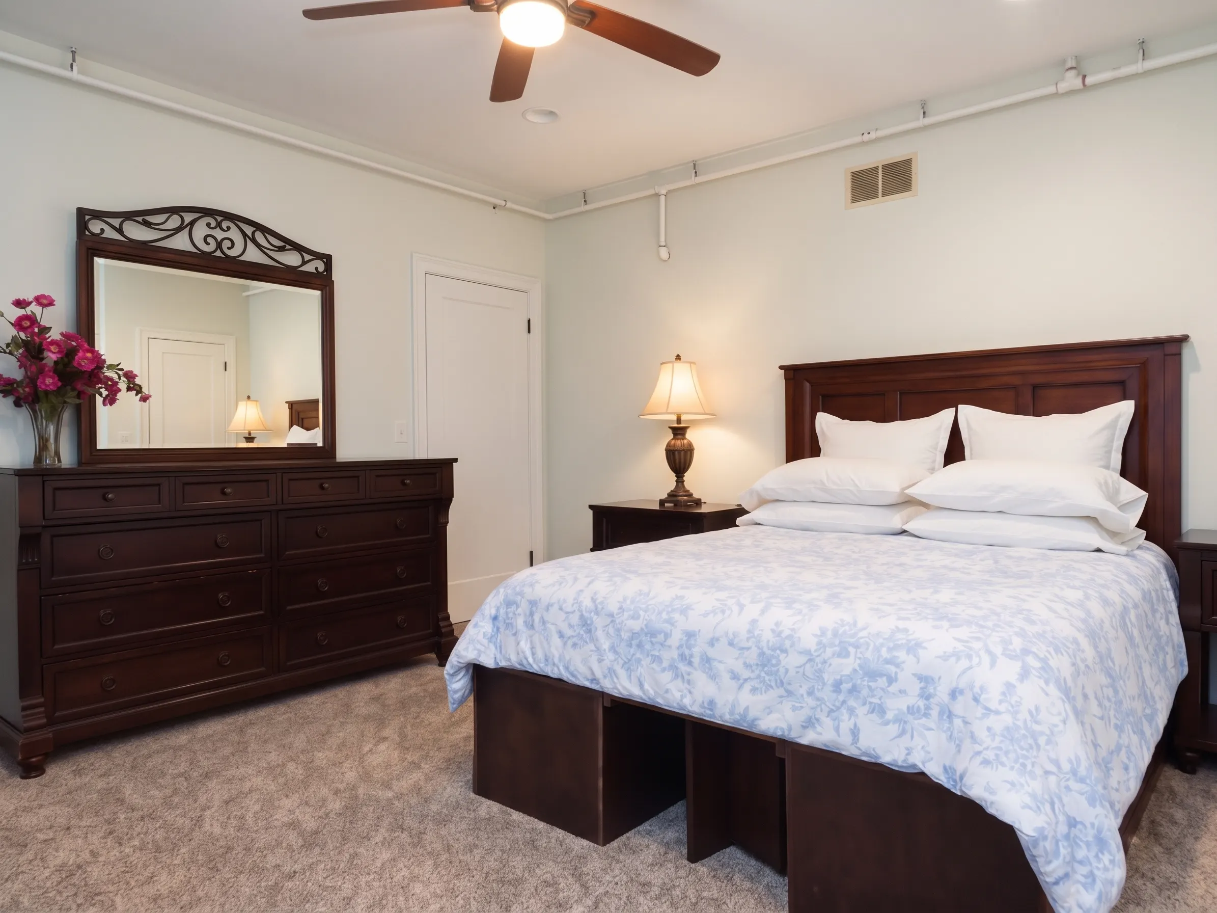Lower level queen bedroom with floral bedding, dresser, and mirror