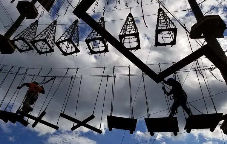 Climbers crossing hanging obstacles at the Monkey Business adventure park, silhouetted against the sky