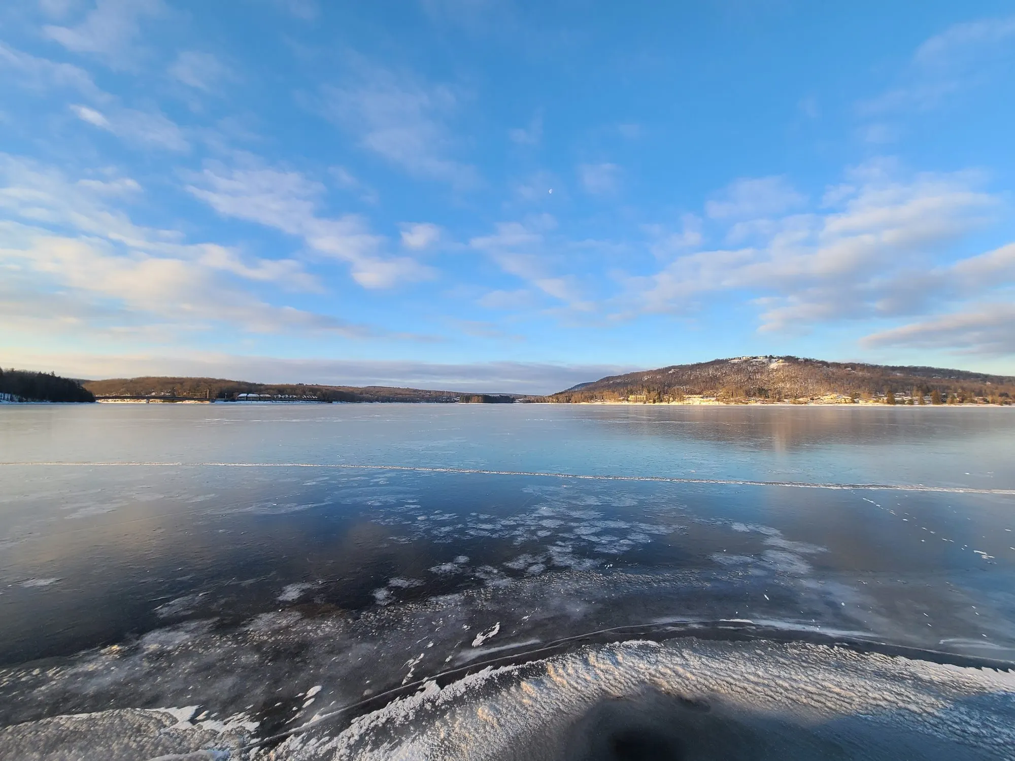 Thin ice spreading across Deep Creek Lake toward distant ridges under a blue winter sky