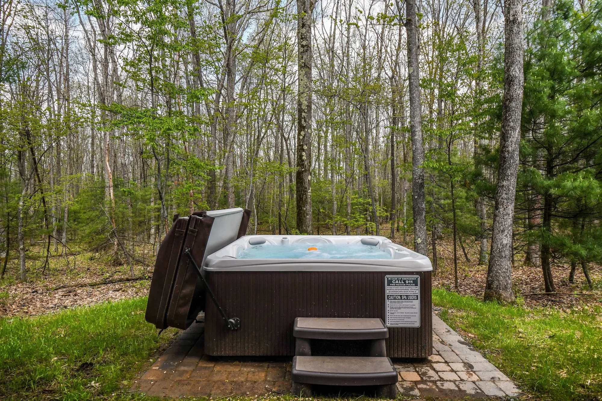 Open-air hot tub on its own stone pad at the edge of the woods