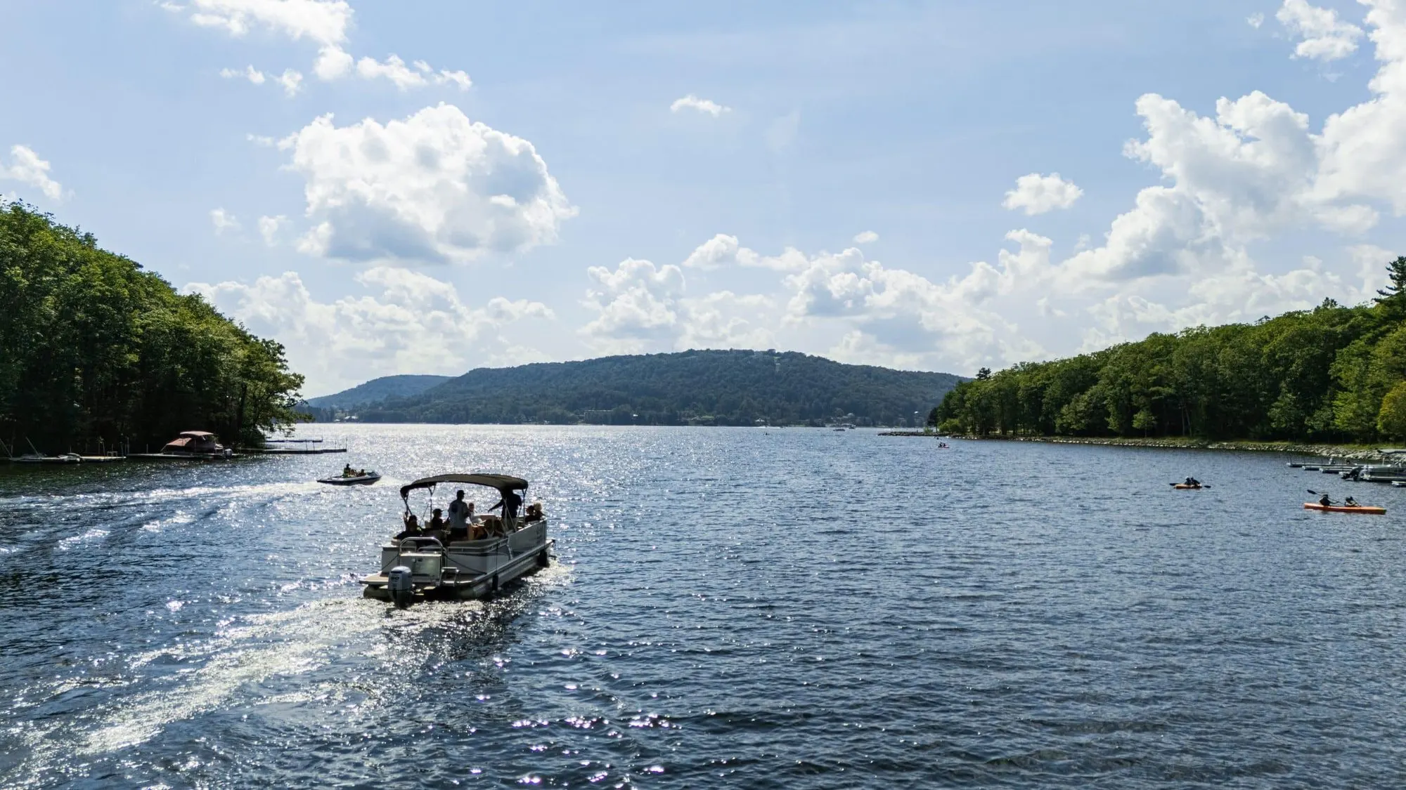 A pontoon boat crossing Deep Creek Lake past wooded shores on a summer day