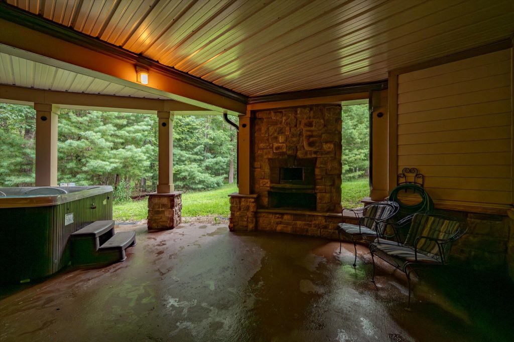 Stone patio on the lower level with outdoor fireplace and woodland backdrop
